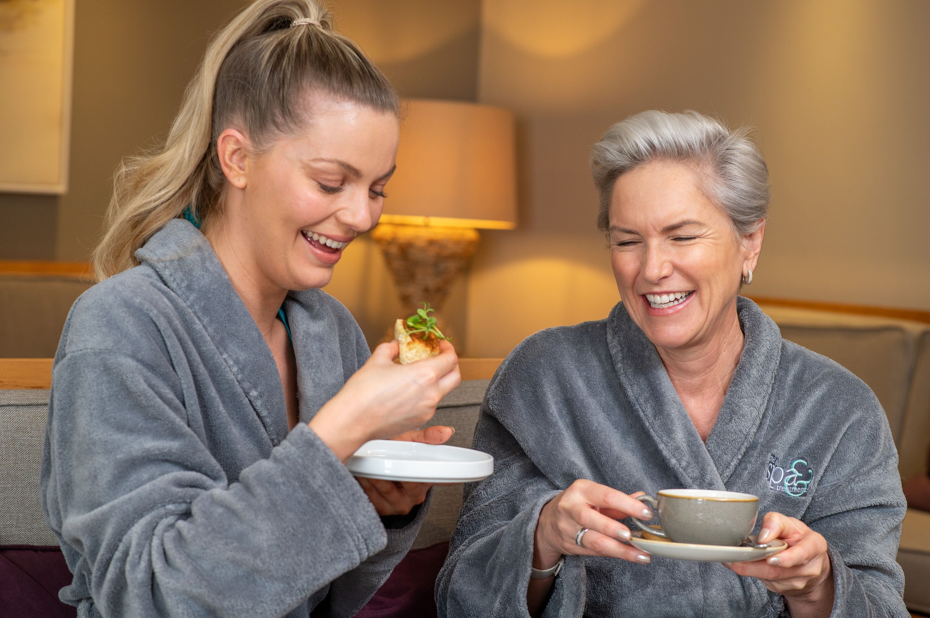 Mother and daughter in bathrobe enjoying a cup of tea and a snack
