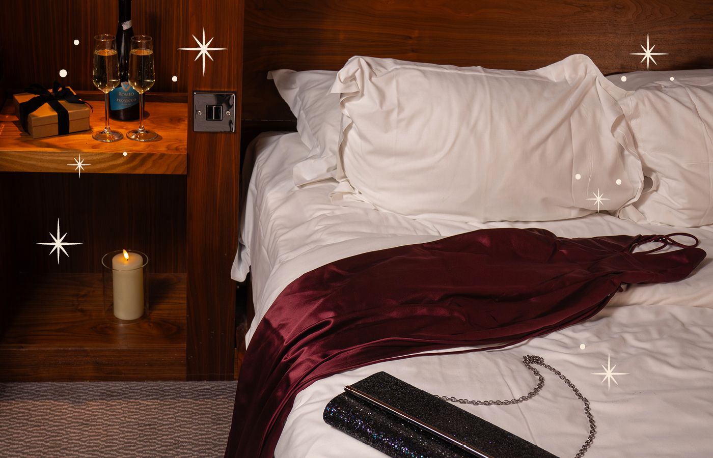 Landscape image of bedroom with red dress on bed, sparkly bag and champagne with glasses with sparkles